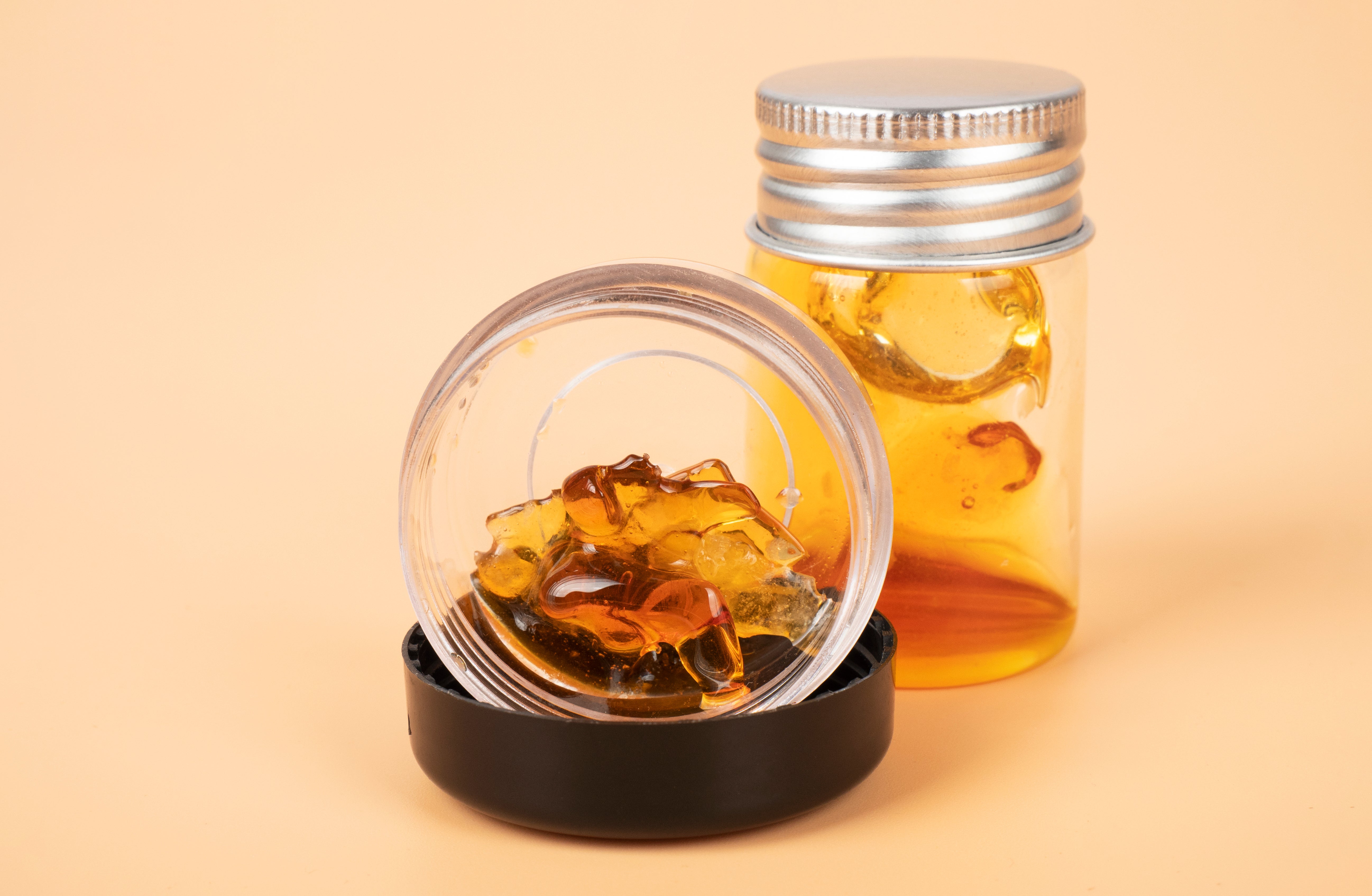 A clear container with amber resin sits on a black base, next to a glass jar with a silver lid filled with similar resin.