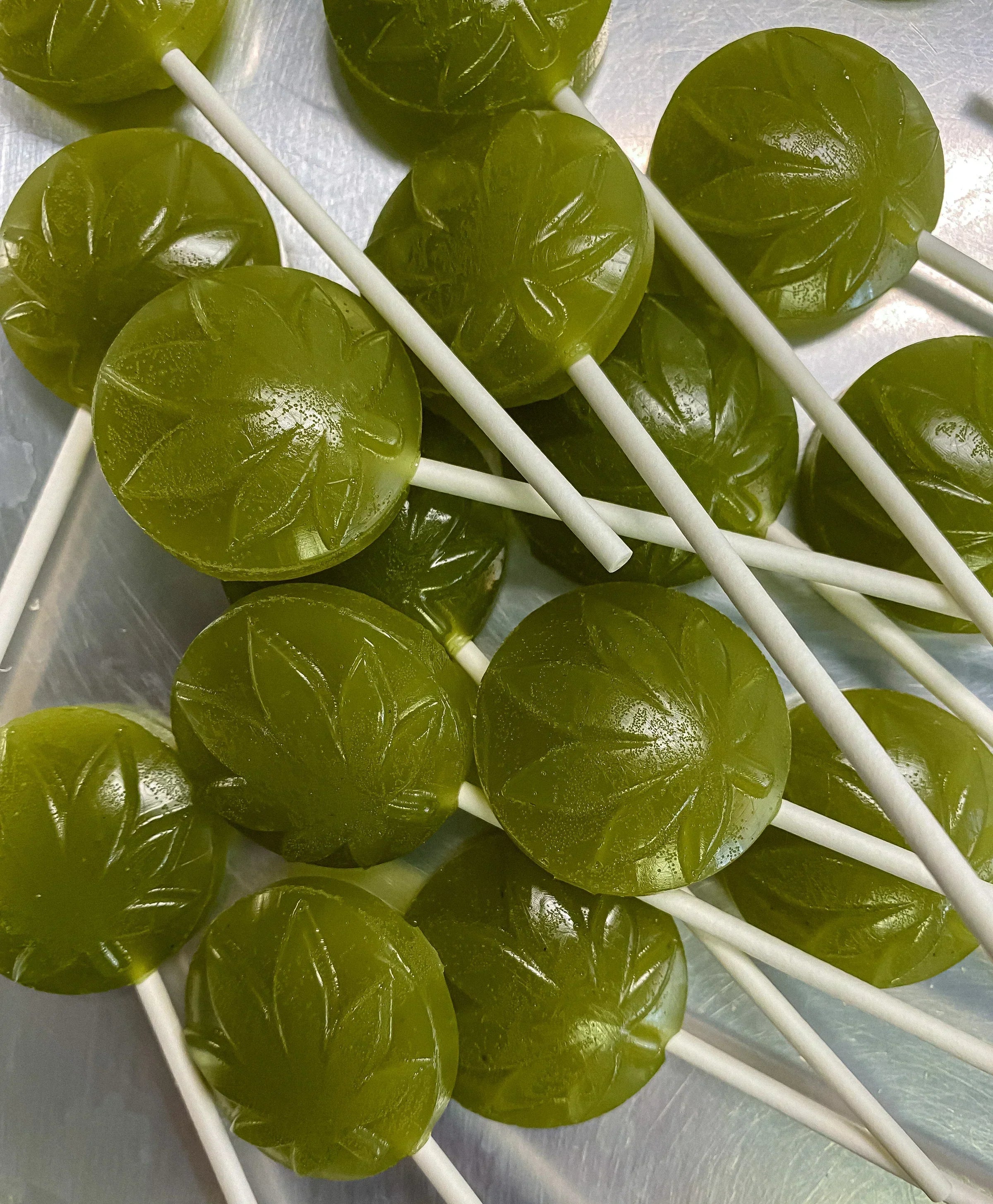 A photograph of a pile of NOVA Hemp cannabis lollies. The THC candy is bright green with white lollipop sticks.