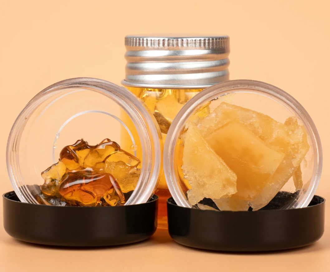 Three clear containers with different types of cannabis concentrate. One has amber-colored wax, one has solid golden chunks, and the third holds a golden liquid. 