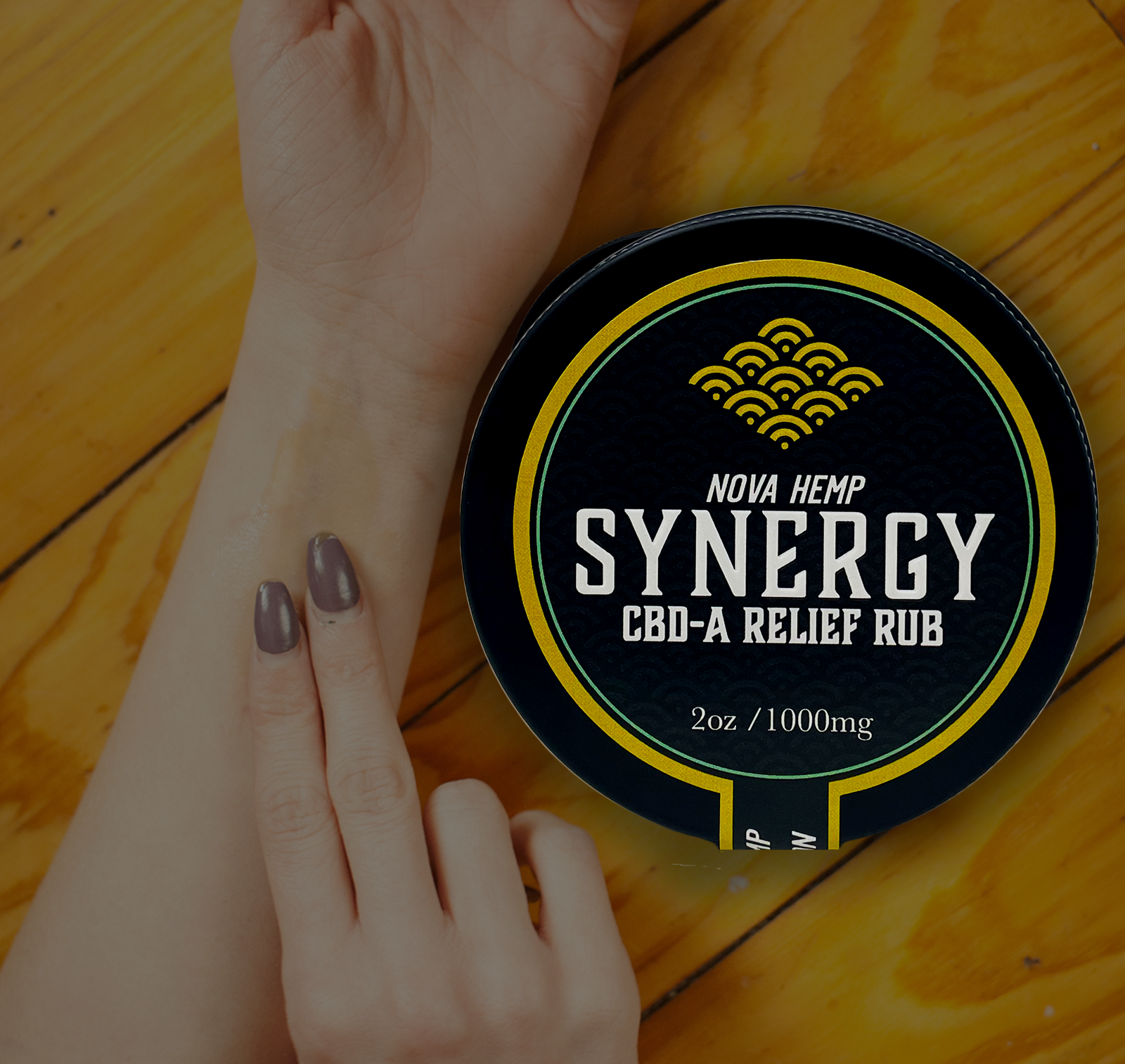 A hand applying Nova Hemp Synergy CBD-A Relief Rub to the wrist on a wooden surface. 