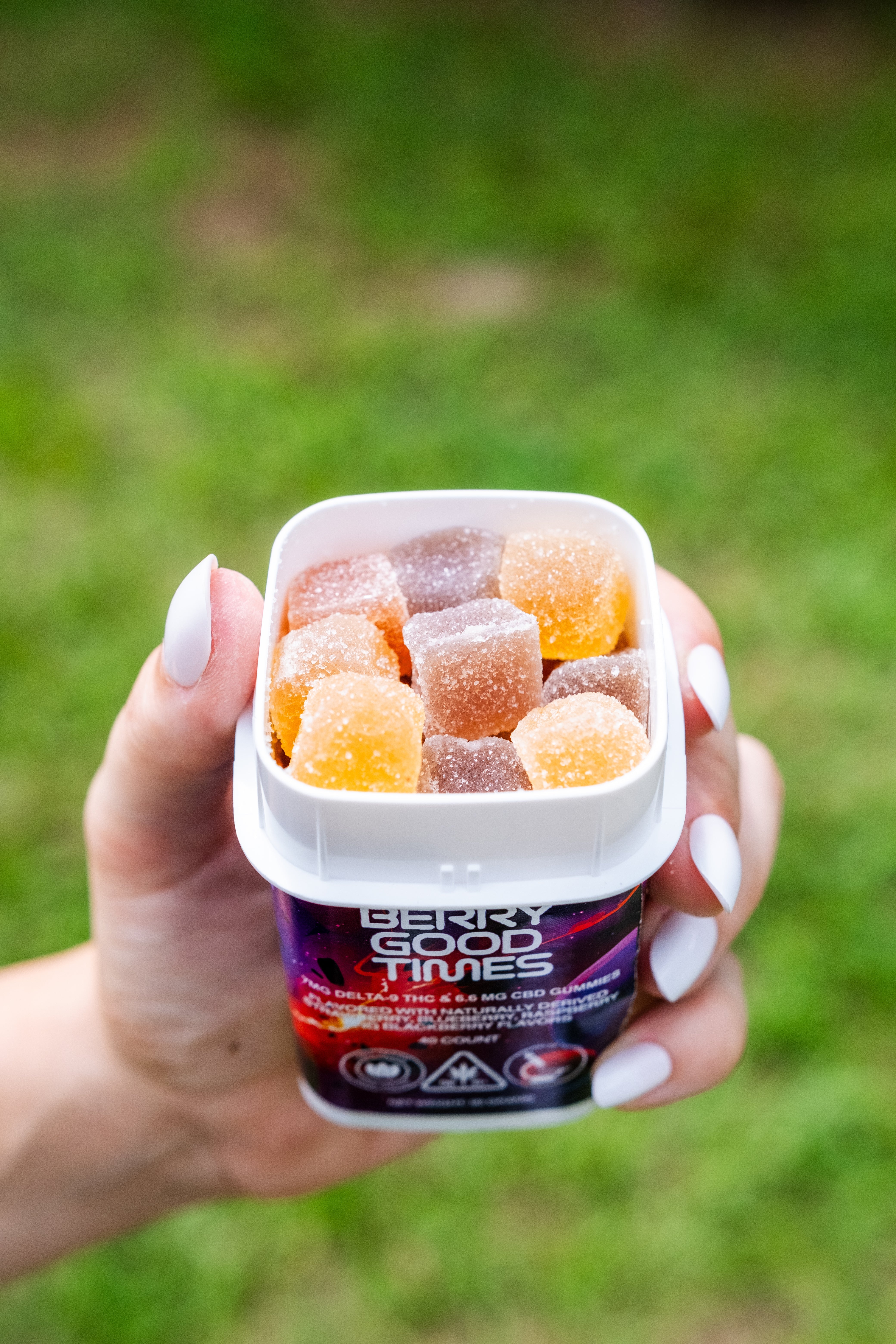 A hand holding a container of gummy candies in various colors, labeled Berry Good Times. 