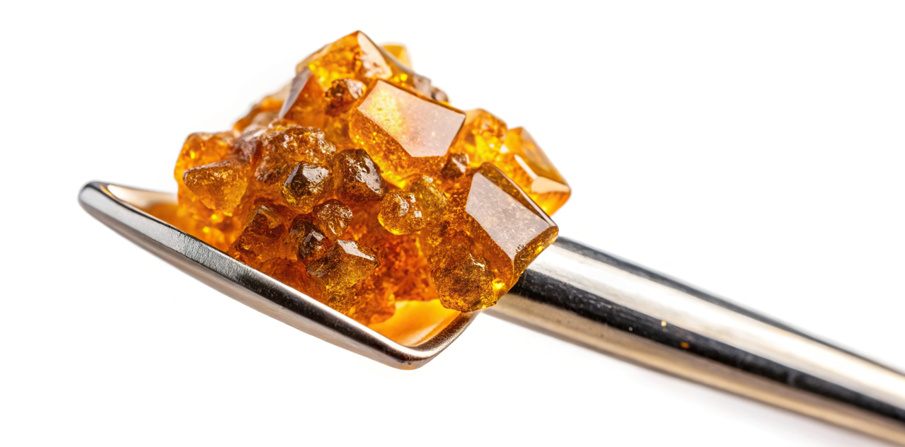 A shiny amber-colored sugar crystal on a silver spoon against a white background. 