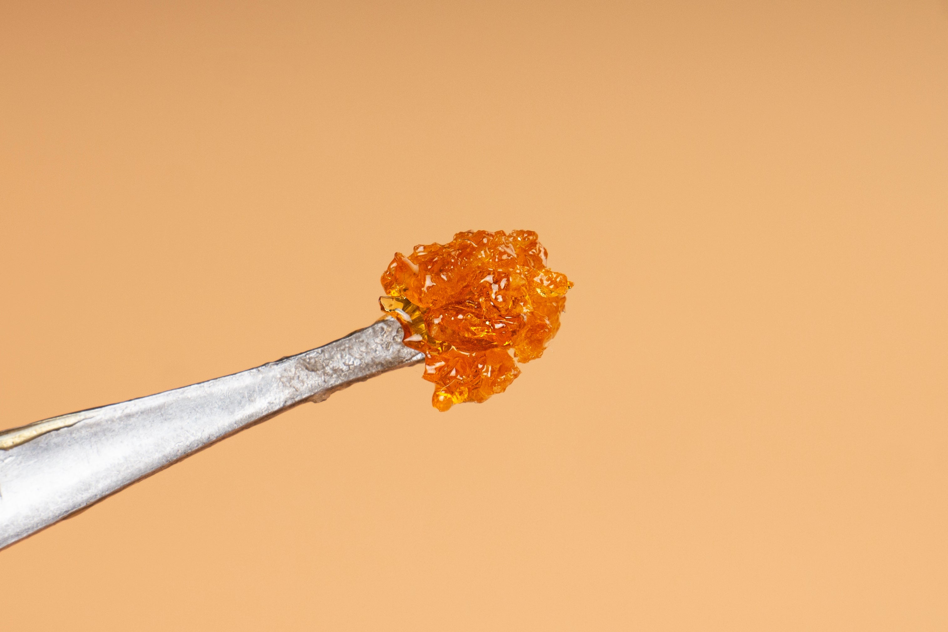 A glistening orange resin crystal held by silver tweezers against a light orange background. 